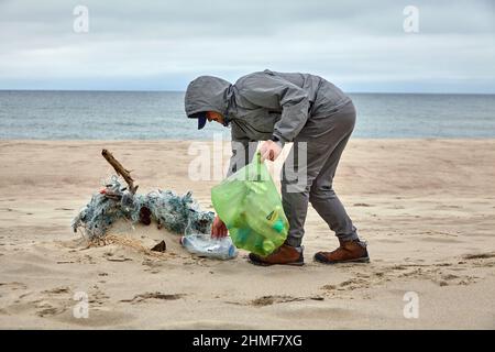 Männlicher Freiwilliger sammelt Trümmer, die von einem Sturm auf einen Sandstrand geworfen werden Stockfoto