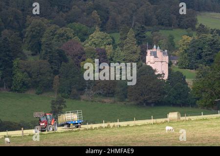 Ein Bauer lädt Hay-Ballen auf einen Anhänger vor Craigievar Castle in Aberdeenshire im Herbst Stockfoto