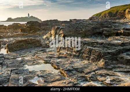 Im Hochsommer warmer Sommernachmittag, in der Nähe des Sonnenuntergangs, unter den Klippen entlang der nordkornischen Küste, dramatische Granit- und Schieferfelsen und Leuchtturm Stockfoto