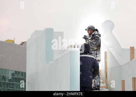 Ein Arbeiter in einer Winterjacke mit Kapuze und einer Strickmütze aus Wolle mit Visier am Arbeitsplatz Stockfoto