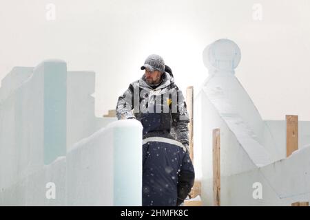 Ein Arbeiter in einer Winterjacke mit Kapuze und einer Strickmütze aus Wolle mit Visier am Arbeitsplatz Stockfoto