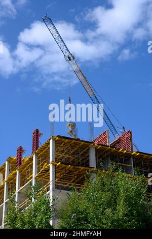 Der Boom eines Krans, der Beton auf den Bau eines Hochhauses speist, vor dem Hintergrund eines blauen Himmels mit Wolken Stockfoto