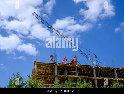 Der Boom eines Krans, der Beton auf den Bau eines Hochhauses speist, vor dem Hintergrund eines blauen Himmels mit Wolken Stockfoto