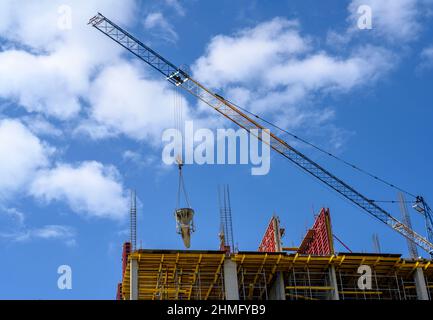 Der Boom eines Krans, der Beton auf den Bau eines Hochhauses speist, vor dem Hintergrund eines blauen Himmels mit Wolken Stockfoto