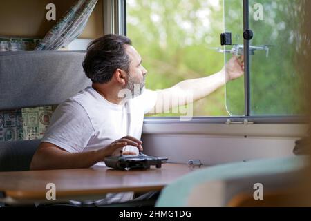 Reisemobil-Reisekonzept. Mann steuert eine Drohne.ein Mann steuert eine Drohne vom Fenster eines Wohnmobils aus Stockfoto