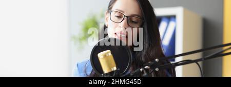 Junge schöne Frau spricht am Arbeitsplatz ins Mikrofon Stockfoto