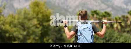 Der Mann steht mit dem Rücken und hält skandinavische Stöcke auf dem Berg Stockfoto