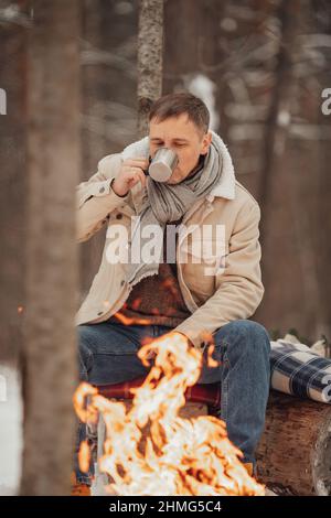 Ein Mann im Winterwald am Feuer gießt Kaffee Stockfoto