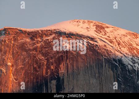 Das letzte Licht der untergehenden Sonne beleuchtet eine schneebedeckte Halbkuppel an einem Winternachmittag. Yosemite Nationalpark. Stockfoto