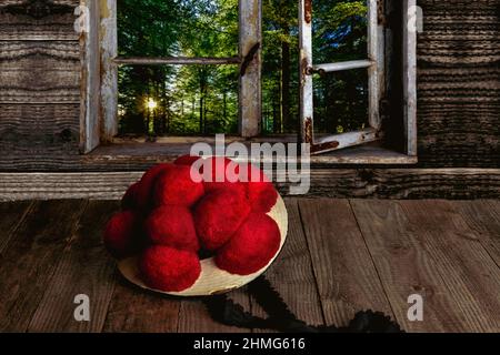 Original Schwarzwälder Bollenhut auf einem Holztisch vor einem Holzfenster mit Blick auf den Wald liegend Stockfoto
