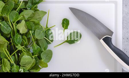 Babyspinat und ein Messer auf einem Schneidebrett. Frische Spinatblätter aus nächster Nähe, flach legen Stockfoto
