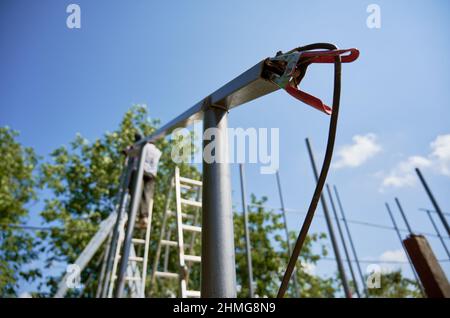 Nahaufnahme der Tragkonstruktion für Photovoltaik-Solarpanel mit elektrischer Schweißklemme. Selektiver Fokus des Metall-Solarpanel-Mastes mit Erdkabelklemme unter schönem blauen Himmel. Stockfoto