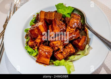 Chinesische tiefgebratene Schweinestückchen mit süßer und saurer Sauce, serviert auf Salatblättern. Hochwertige Fotos Stockfoto