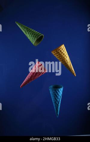 Vier Waffelkegel in verschiedenen Farben schweben vor blauem Hintergrund. Das Bild enthält den Kopierbereich Stockfoto