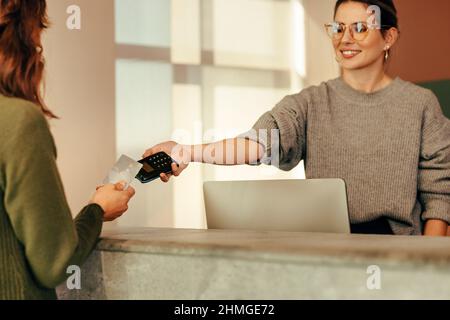 Verkäuferin nimmt eine Kreditkartenzahlung von einer Kundin an. Die glückliche Inhaberin eines kleinen Unternehmens lächelte fröhlich, während sie ihrem Kunden bei der half Stockfoto