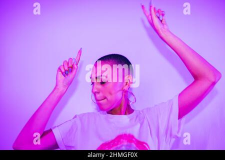 Hipster-Frau, die auf einer Hausparty zu ihrem Lieblingslied tanzt. Lebendige junge Frau, die allein in hellem Neonlicht steht. Junge Frau mit Spaß ein Stockfoto