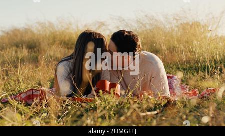 Das Paar, das auf dem Gras liegt, küsst sich gegenseitig Stockfoto