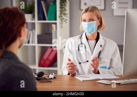 Ältere Weibliche Arzt In Weißem Mantel Trägt Gesichtsmaske Mit Treffen Mit Frau Patient Im Büro Stockfoto