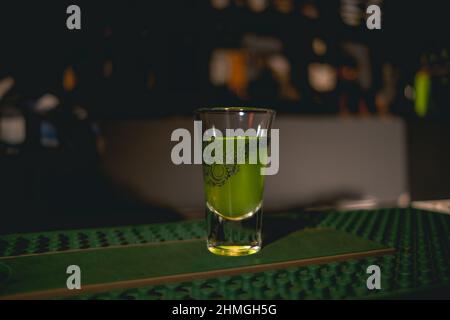 Schnapsglas mit grünem Getränk auf Gummimatte an der Theke Stockfoto