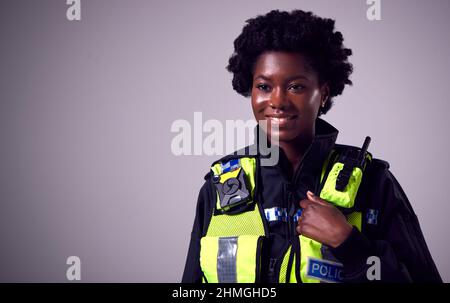Studio Portrait Of Smiling Young Female Police Officer Against Plain Background Stockfoto