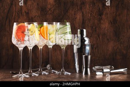 Gin und Tonic-Cocktails werden serviert. Alkoholische Getränke mit Limette, Zitrone, Grapefruit, Gurke, Soda und würzigen Kräutern in Weingläsern, Holzhintergrund. Sommer Stockfoto