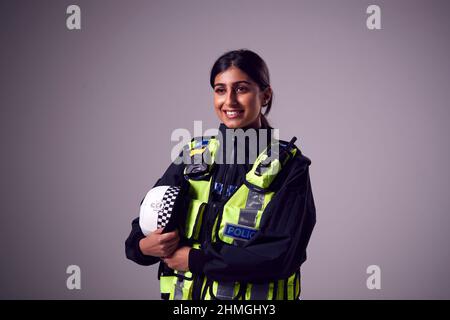 Studio Portrait Of Smiling Young Female Police Officer Against Plain Background Stockfoto