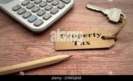 Text zur Grundsteuer auf Schlüsselanhänger mit Taschenrechner, Bleistift und Holzschreibtischhintergrund. Konzept der Immobiliensteuer. Stockfoto