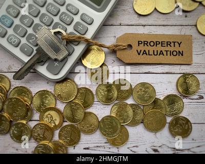 Text zur Bewertung von Immobilien auf Schlüsselanhänger mit Taschenrechner, Münzen und weißem Holzschreibtisch. Stockfoto