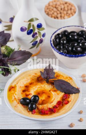 Gesundes Frühstück mit hausgemachtem Hummus und schwarzen Oliven auf weißem Holzhintergrund. Ernährung und gesunde Snacks. Stockfoto