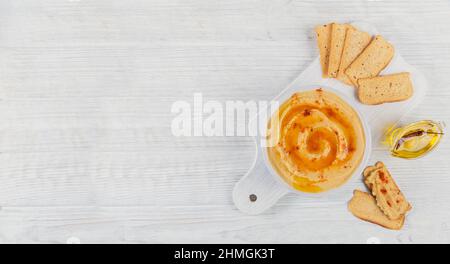 Gesunder hausgemachter cremiger Hummus mit Olivenöl und Knäckebrot auf weißem Holzhintergrund. Gesunde Ernährung und Konzept der Ernährung. Stockfoto