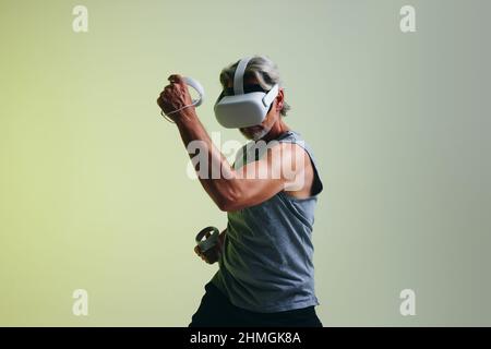 Reifer Mann, der Spiele spielt, während er ein Virtual-Reality-Headset trägt. Mann genießt eine 3D Simulation, während er vor einem Studiohintergrund steht. Stockfoto