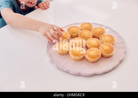 Nahaufnahme Von Boy, Der Frisch Gebackenen Hausgemachten Cupcake Von Plate In Kitchen At Home Mitnimmt Stockfoto