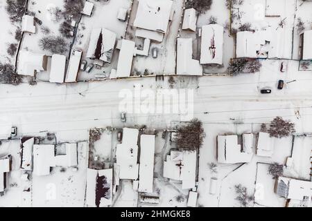 Blick von oben auf die Straße mit Häusern im schneebedeckten Dorf am Wintertag nach Schneefall Stockfoto