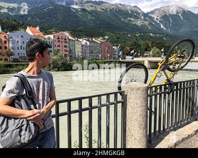 Ein asiatischer Tourist steht am Inn in Innsbruck. Er schaut auf ein Geländer, auf dem ein umgedrehten Fahrrad geparkt ist. Stockfoto