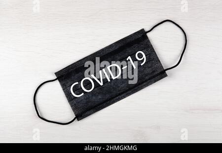 Schwarze medizinische Maske mit Aufschrift covid-19 auf dem Tisch Stockfoto