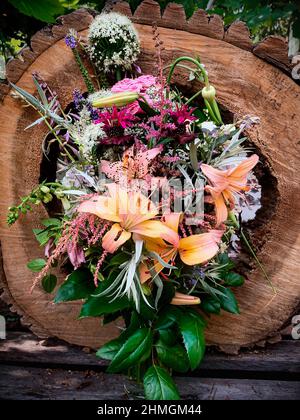 Romantischer Strauß in einer Vase, die aus altem Baum geschnitten wurde. Die Zusammensetzung umfasst Lilie, Fuchshandschuh, Allium, Astilbe, Monarden, rosen, veronica, Knoblauchpfeile, Wurmw Stockfoto