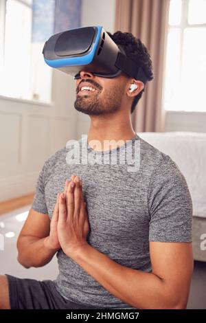Mann Mit Virtual Reality-Headset Und Ohrhörern Auf Yogamatte Im Schlafzimmer Zu Hause Sitzen Stockfoto