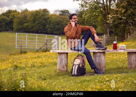 Mann, Der Auf Der Bank Auf Dem Land Sitzt Und Musik Oder Podcast Über Kabellose Kopfhörer Hören Kann Stockfoto