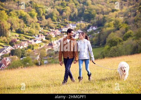 Paar Mit Pet Golden Retriever Hund Zu Fuß Entlang Pfad Über Feld In Der Landschaft Stockfoto