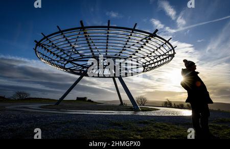 Haslingden, Lancashire, Großbritannien, Mittwoch, 09. Februar 2022. Ein Spaziergänger hält an, um die untergehende Sonne am Halo panopticon über der Stadt Haslingden zu bewundern, Stockfoto