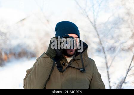 Ein Mann mit Wintermütze und Fäustlingen schießt mit einer digitalen Spiegelreflexkamera, während er im Freien steht Stockfoto