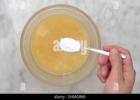 Draufsicht auf Frau Hand, die Backpulver in den Teig in Glasschüssel als Zutat von Kuchen medovik auf Marmor Hintergrund Stockfoto