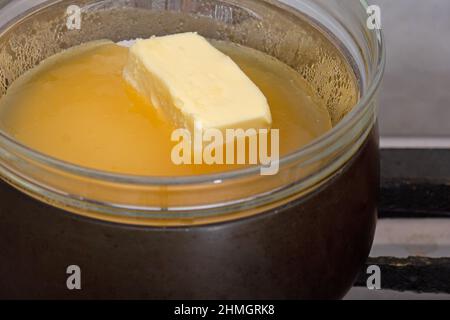 Bain-marie mit Zucker, Butter und Honig in Glasschüssel auf Kochtopf als Zutaten für Kuchen medovik auf Herd Stockfoto