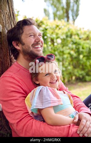 Liebevoller Vater Kuscheltierend Junge Tochter Sitzt Unter Baum Im Garten Zusammen Stockfoto