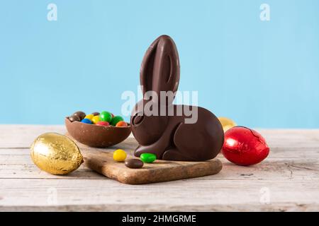 Osterschokoladenhase und bunte Eier auf Holztisch und blauem Hintergrund Stockfoto