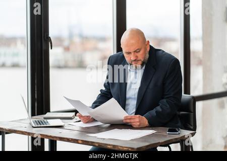 Fokussierter reifer Geschäftsmann in Anzug unterzeichnet Dokumente, unterzeichnet Vertrag Stockfoto