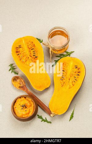Hälften von rohem Kürbis mit Butternusskürbis-Püree, Honig und frischen Kräutern. Sortiment Zutaten zum Kochen, Steinbeton Hintergrund, Draufsicht Stockfoto