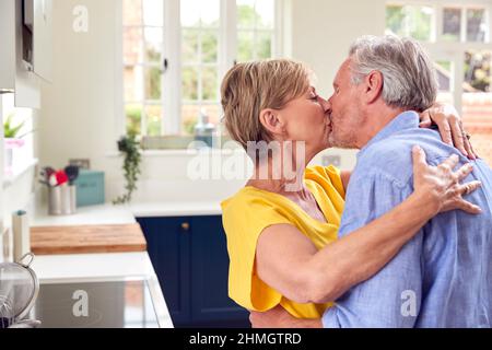 Liebevolles Rentnerpaar Umarmt Und Küsselt In Der Küche Zu Hause Zusammen Stockfoto