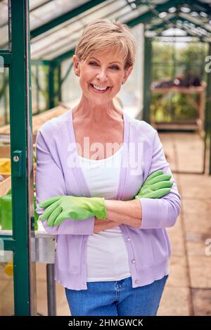 Porträt Einer Älteren Frau Mit Gartenhandschuhen, Die Im Torway Des Gewächshauses Steht Stockfoto