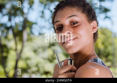 Nahaufnahme einer schönen jungen argentinischen Brünette mit kurzen Haaren, die ein Notizbuch umarmt, die Kamera anschaut und fröhlich lächelt, im Freien in einem p Stockfoto